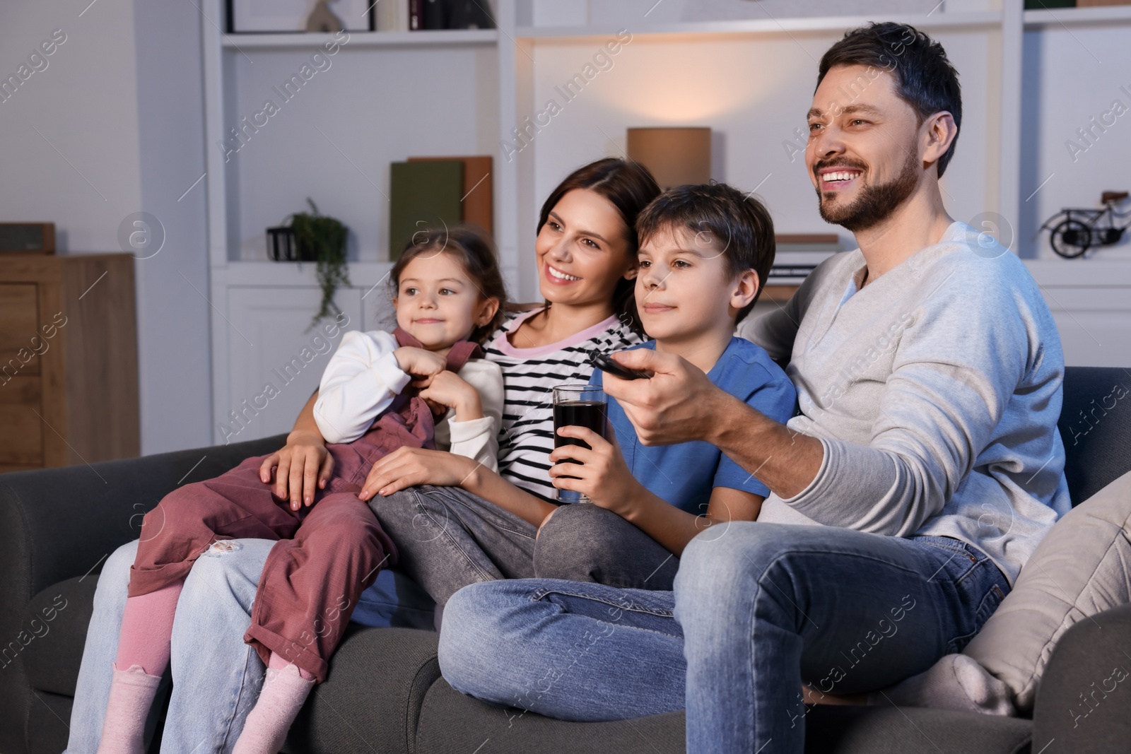 Photo of Happy family watching TV at home in evening. Father changing channels with remote control