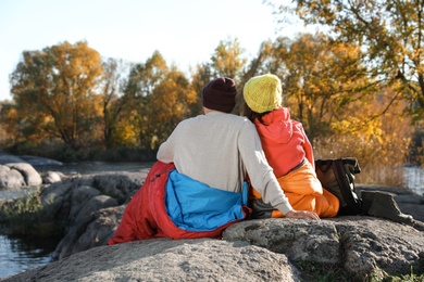 Photo of Couple of campers in sleeping bags sitting on rock