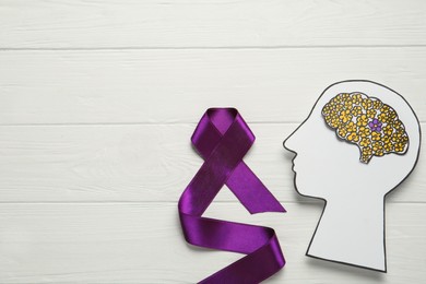 Photo of Top view of human head cutout with brain and purple ribbon on white wooden background, space for text. Epilepsy awareness