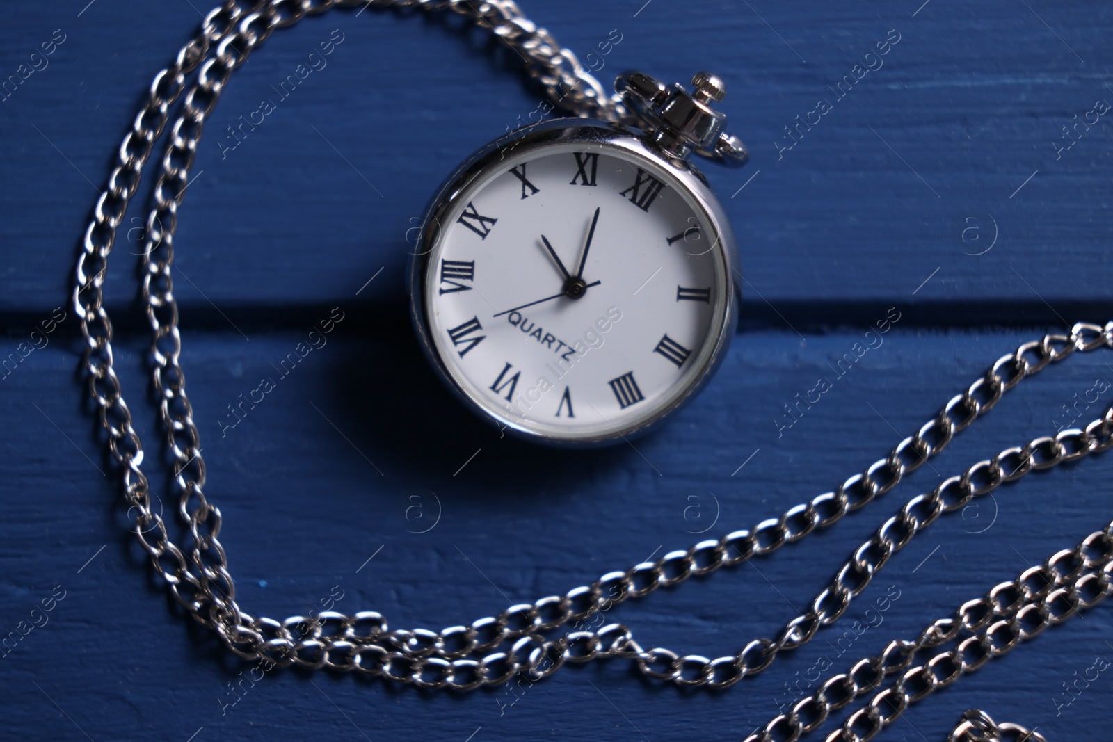 Photo of Silver pocket clock with chain on blue wooden table, top view