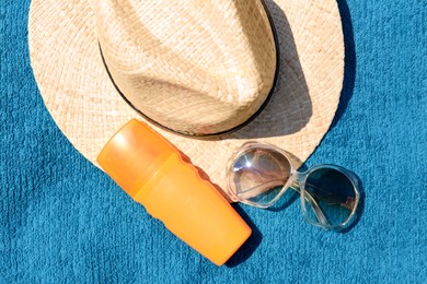 Photo of Stylish straw hat, bottle of sunblock and sunglasses on soft blue beach towel, flat lay