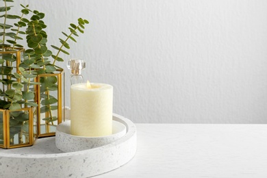 Photo of Stylish tender composition with burning candle and plants on white wooden table against light background, space for text. Cozy interior element