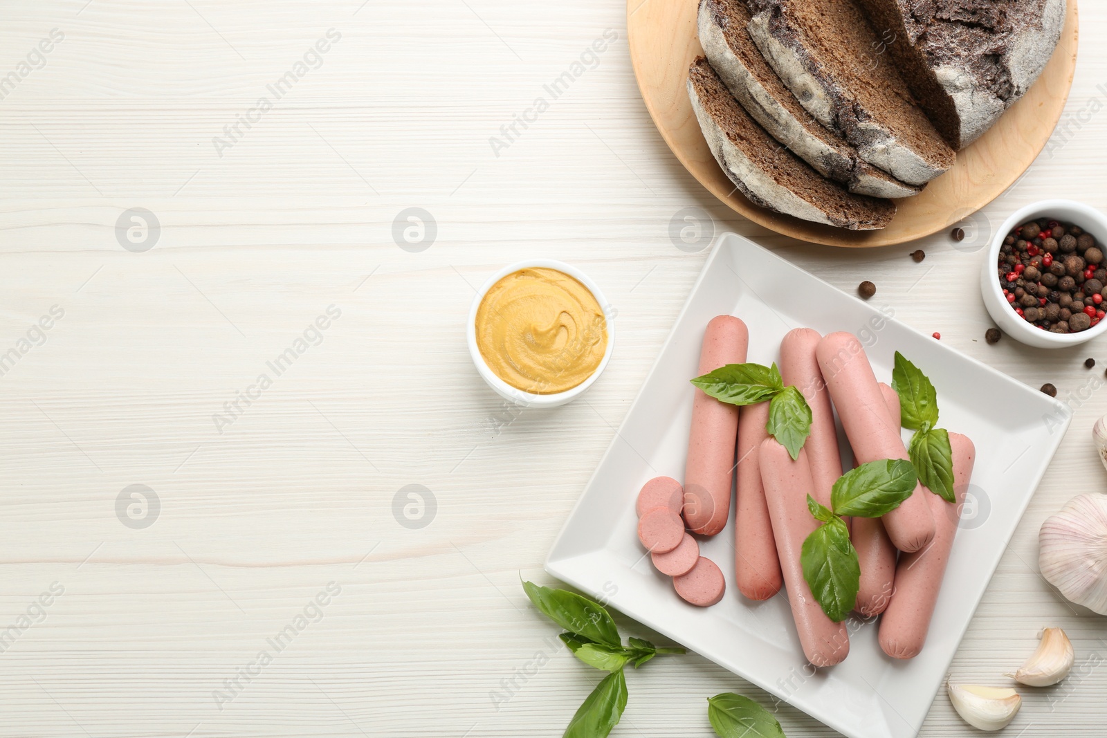 Photo of Fresh raw vegetarian sausages with basil, garlic and sauce on white wooden table, flat lay. Space for text