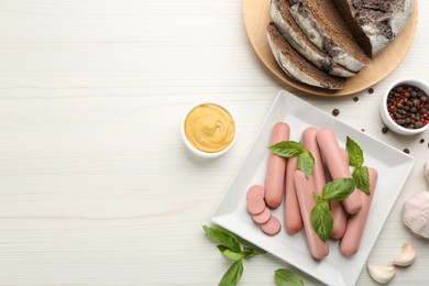 Photo of Fresh raw vegetarian sausages with basil, garlic and sauce on white wooden table, flat lay. Space for text