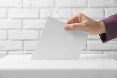 Photo of Woman putting her vote into ballot box against brick wall, closeup