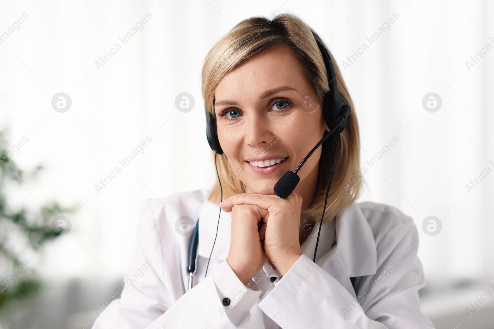 Photo of Portrait of smiling doctor in headphones having online consultation indoors