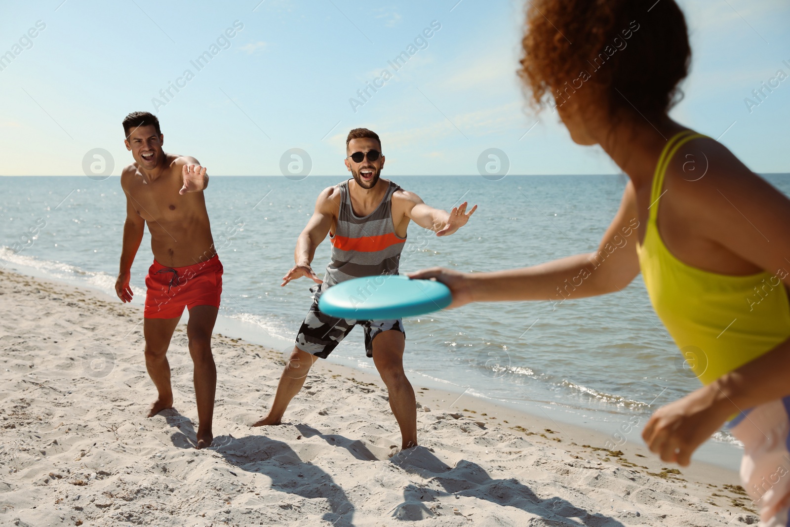 Photo of Friends playing with flying disk at beach on sunny day
