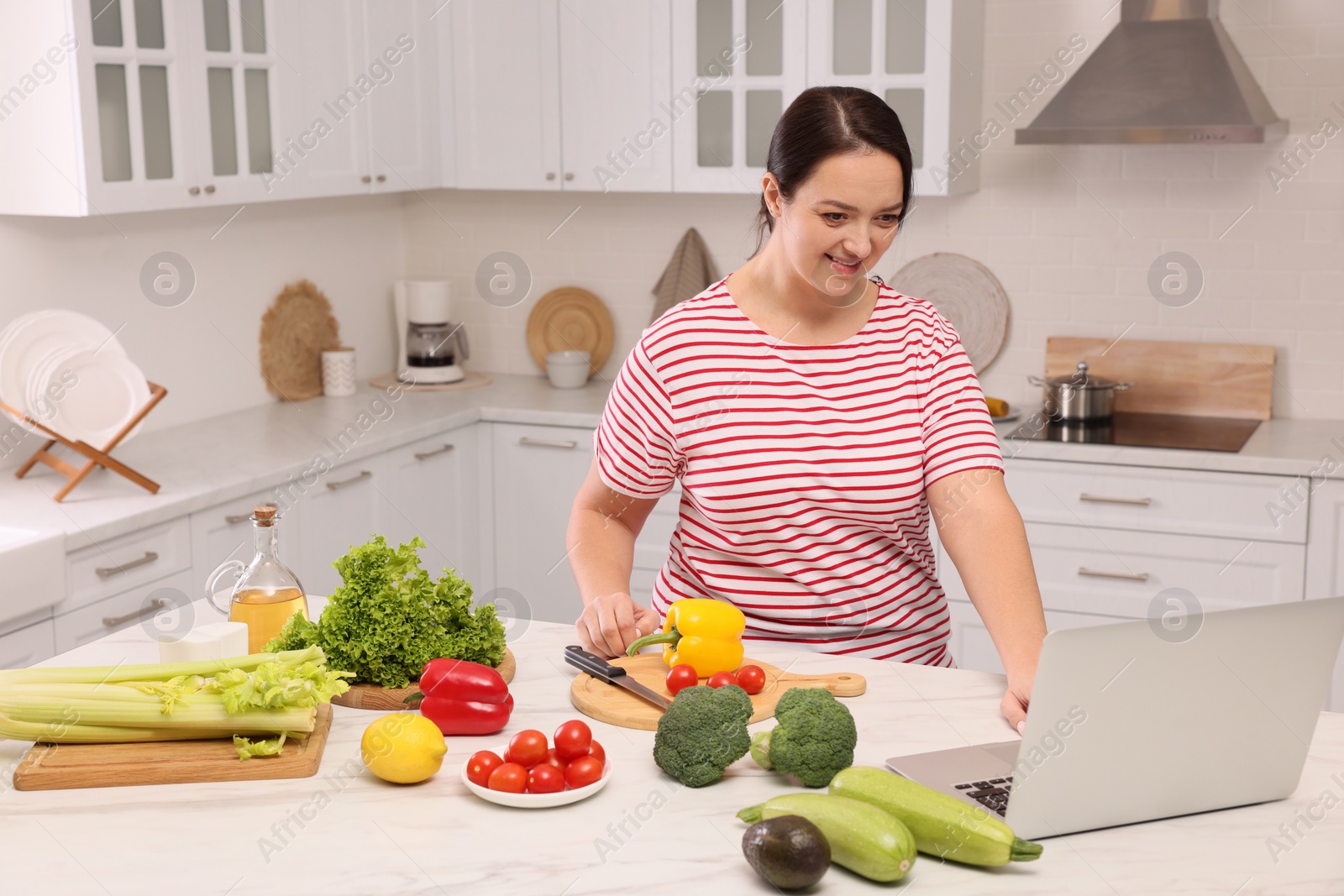 Photo of Beautiful overweight woman following online recipe to prepare healthy meal in kitchen