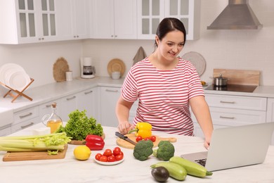 Photo of Beautiful overweight woman following online recipe to prepare healthy meal in kitchen