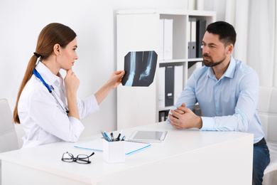 Photo of Orthopedist showing X-ray picture to patient at table in clinic