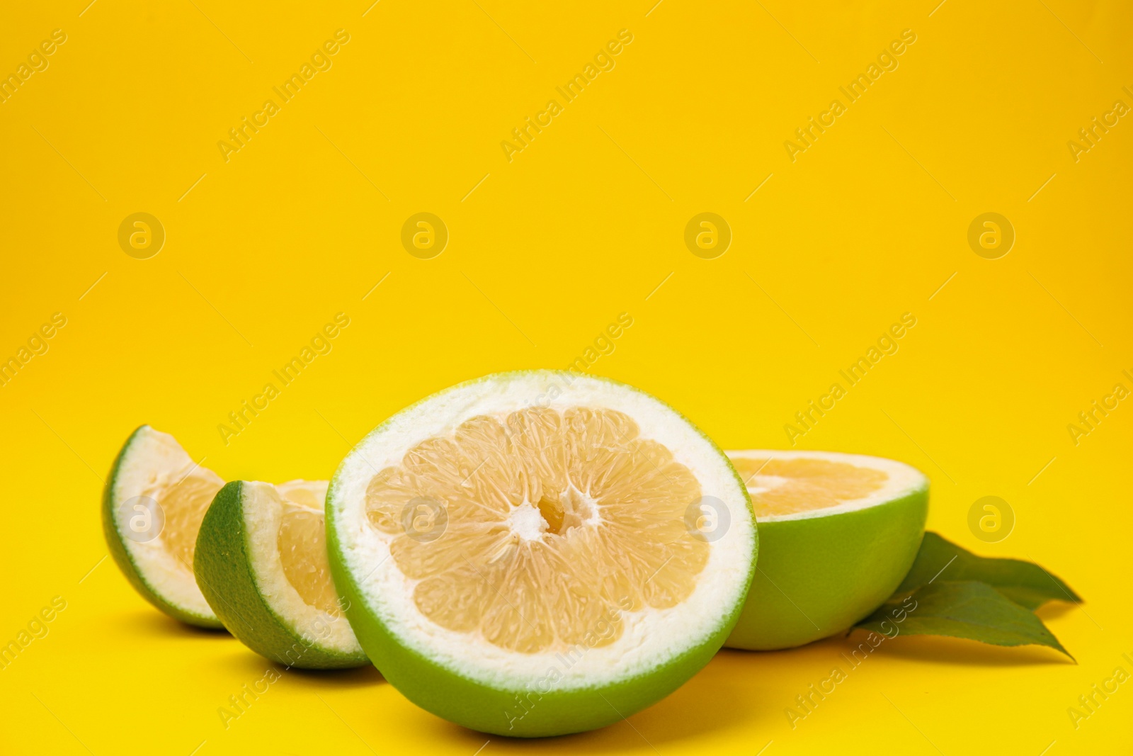 Photo of Cut sweetie fruits with green leaves on yellow background. Space for text