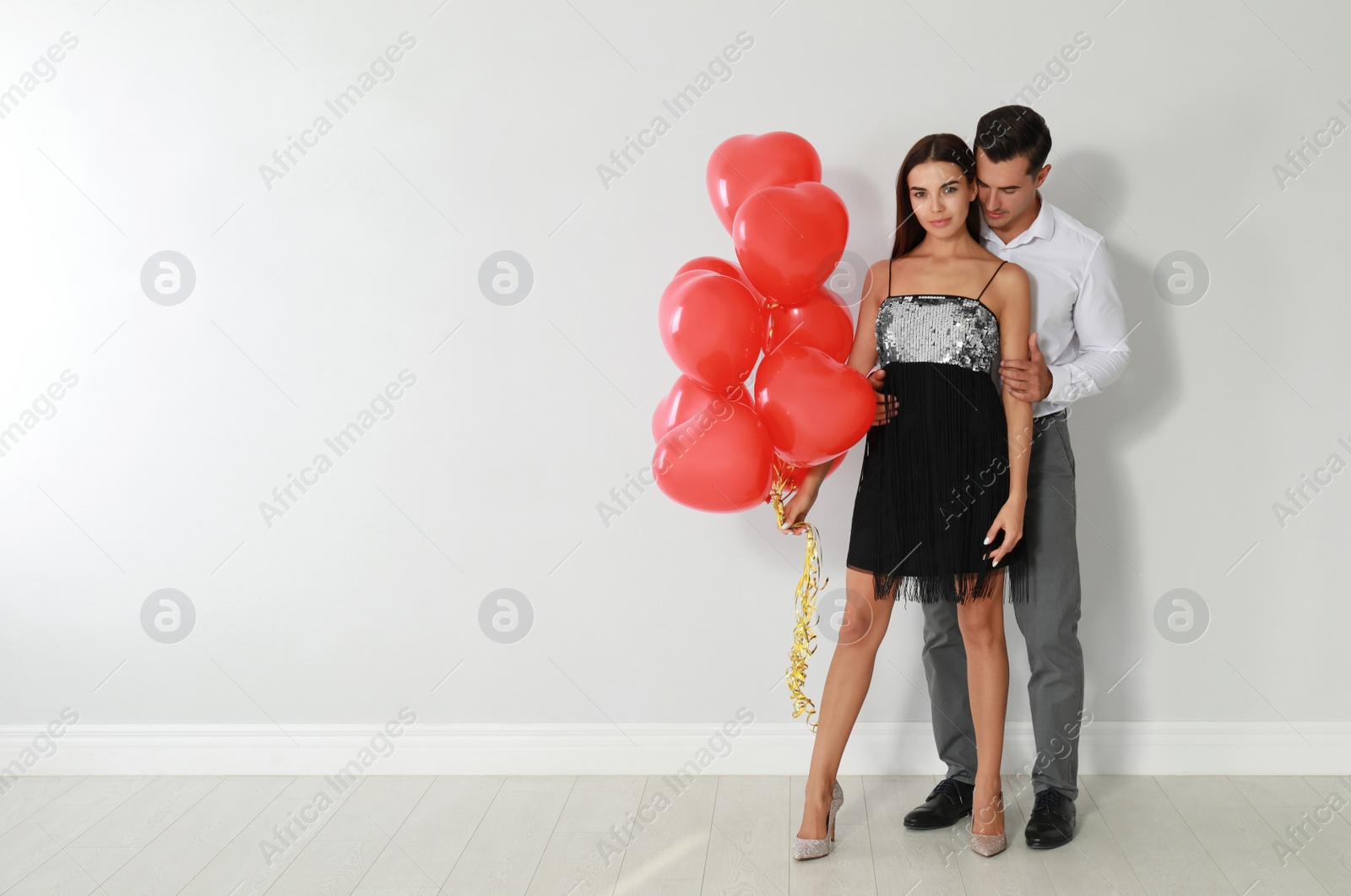 Photo of Beautiful couple with heart shaped balloons near light wall, space for text