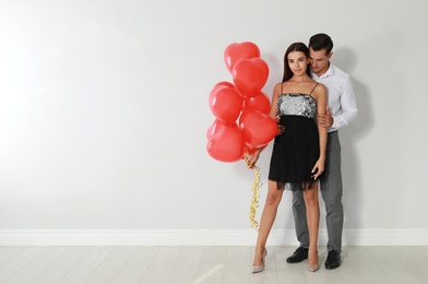 Photo of Beautiful couple with heart shaped balloons near light wall, space for text