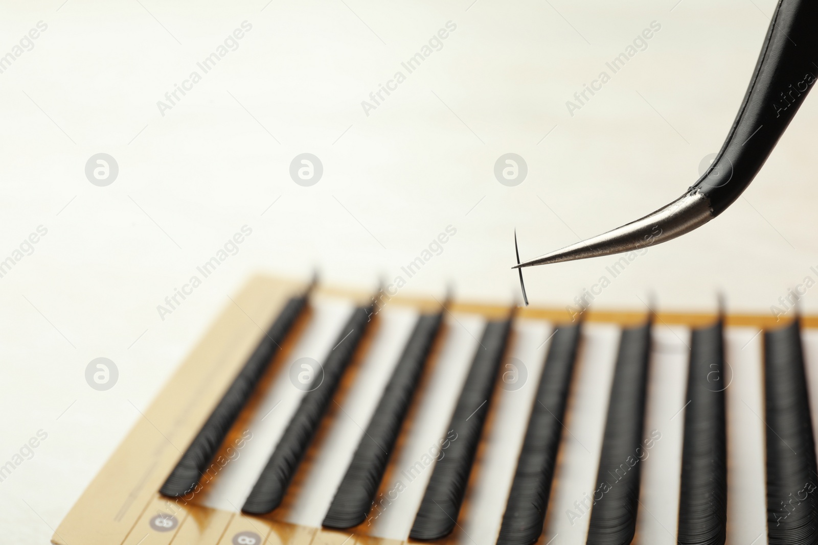 Photo of Tweezers with artificial eyelash on blurred background, closeup. Space for text