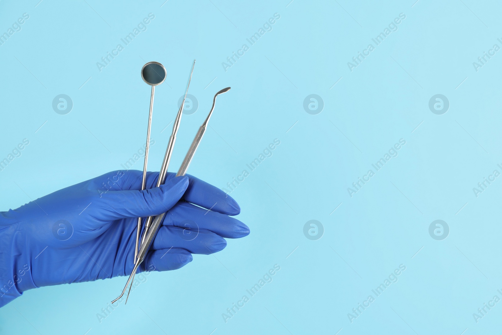 Photo of Dentist holding set of tools on light blue background, closeup. Space for text