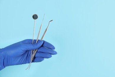 Photo of Dentist holding set of tools on light blue background, closeup. Space for text
