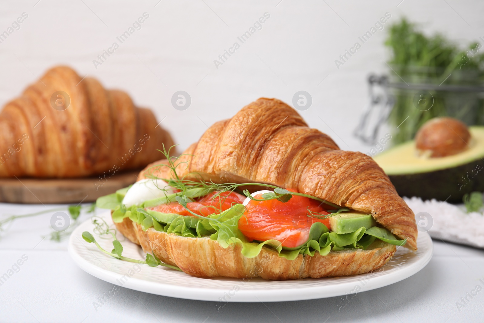 Photo of Tasty croissant with salmon, avocado, mozzarella and lettuce on white table, closeup