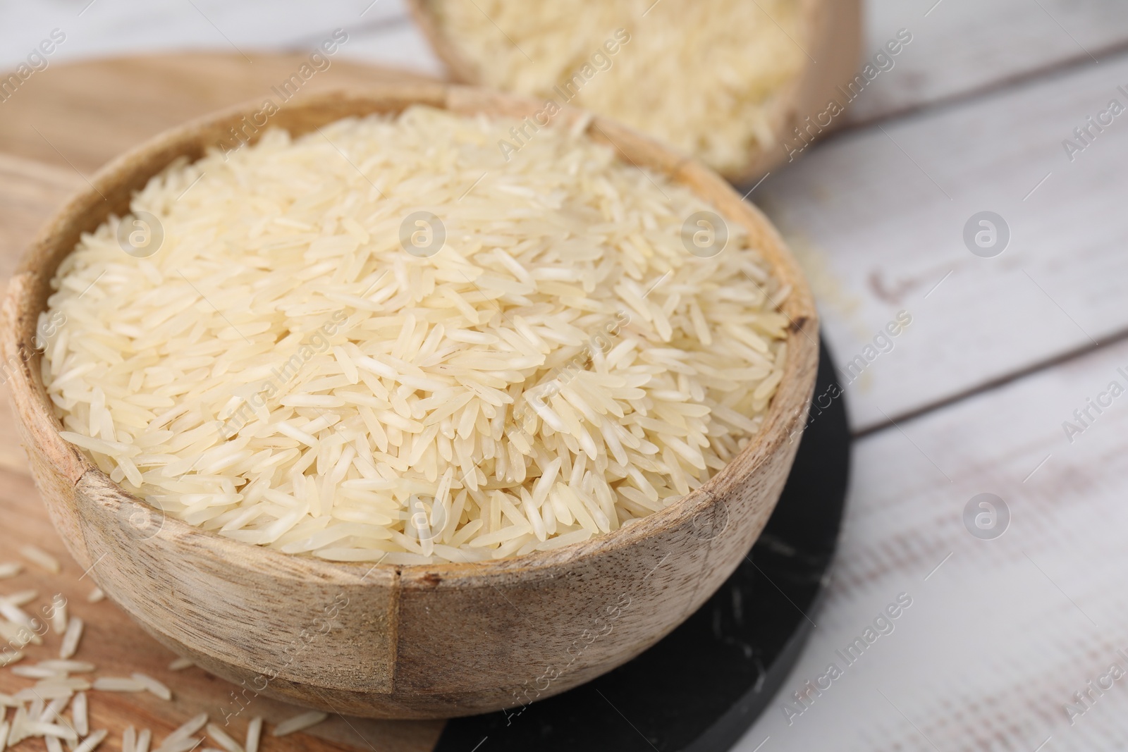 Photo of Raw rice in bowl on light wooden table, closeup. Space for text