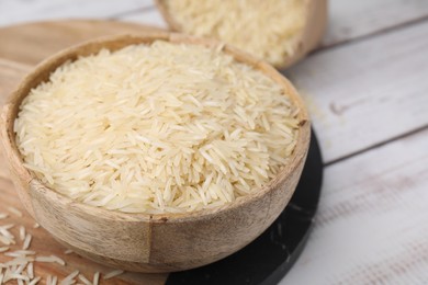 Photo of Raw rice in bowl on light wooden table, closeup. Space for text