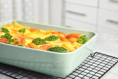 Photo of Tasty broccoli casserole in baking dish on cooling rack, closeup