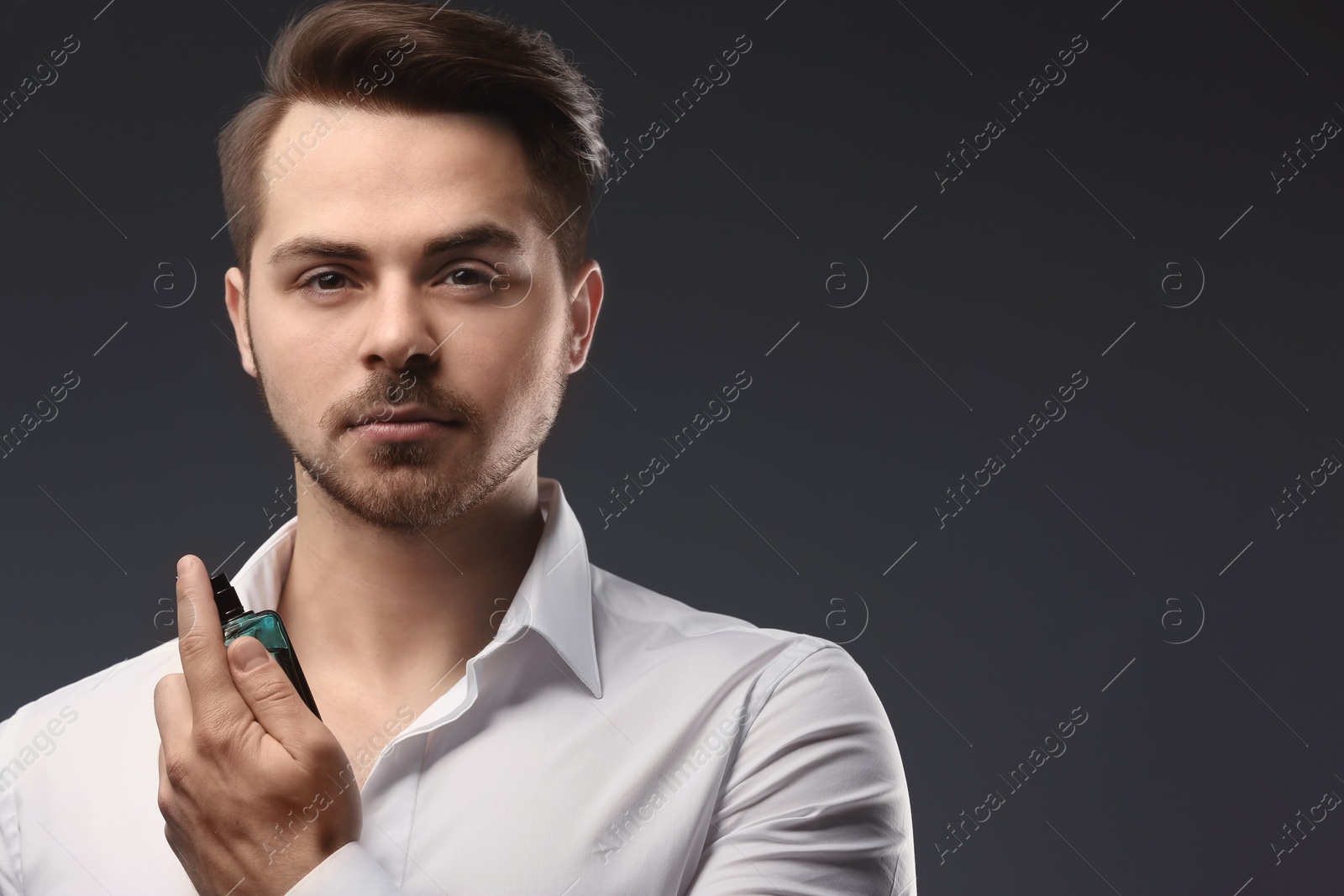 Photo of Handsome man in shirt using perfume on dark background