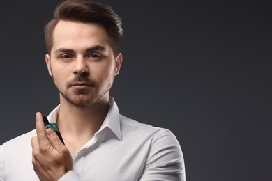 Handsome man in shirt using perfume on dark background