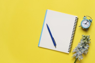 Ballpoint pen, notebook and alarm clock on yellow background, flat lay. Space for text