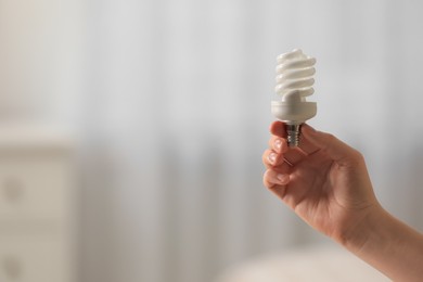 Photo of Woman holding fluorescent light bulb on blurred background, closeup with space for text. Saving energy concept
