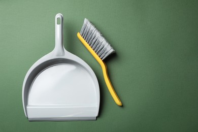 Photo of Plastic hand broom and dustpan on dark green background, flat lay. Space for text