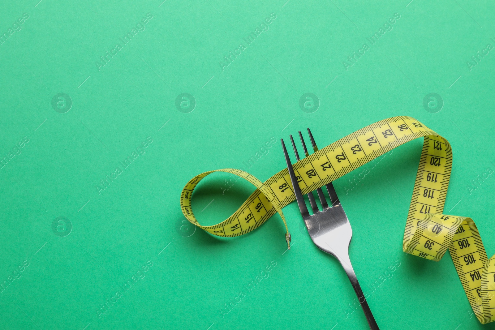 Photo of Fork with measuring tape on green background, top view with space for text. Diet concept