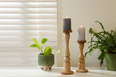 Photo of Pair of beautiful wooden candlesticks and houseplants on white table in room, space for text