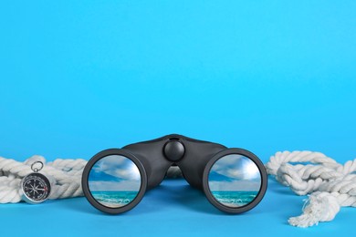 Image of Binoculars, compass and rope on light blue background. Seascape reflecting in lenses