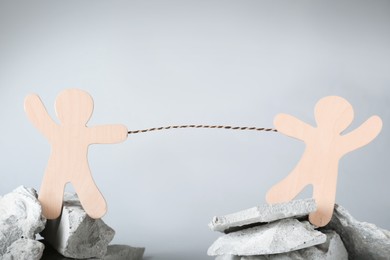 Photo of Competition concept. Wooden human figures on stones tugging rope against grey background