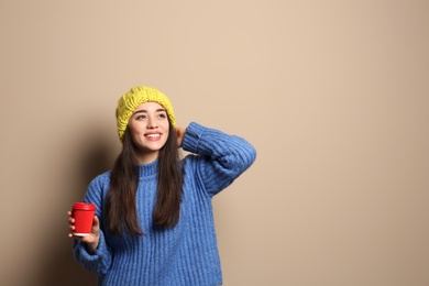 Young woman in sweater with cup of hot coffee on color background, space for text. Winter season