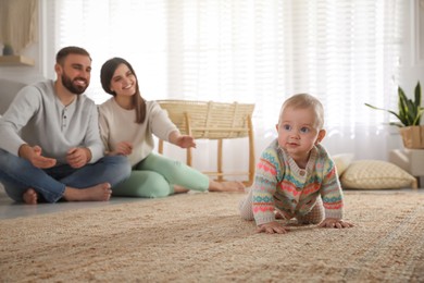 Happy parents watching their baby crawl on floor at home