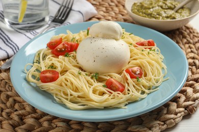 Photo of Plate of delicious pasta with burrata and tomatoes on wicker mat