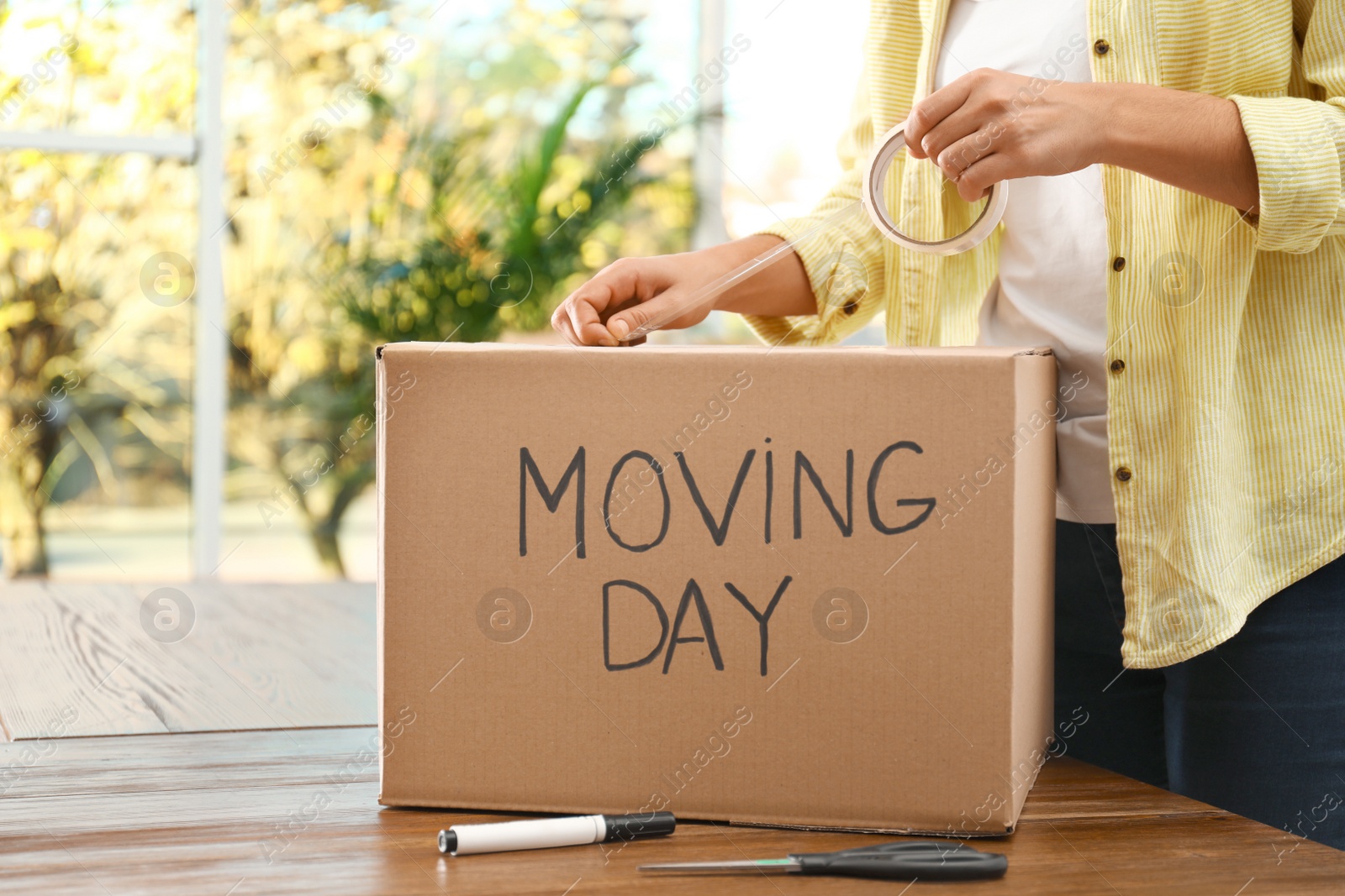 Photo of Woman packing box with words MOVING DAY at wooden table, closeup