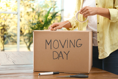 Photo of Woman packing box with words MOVING DAY at wooden table, closeup