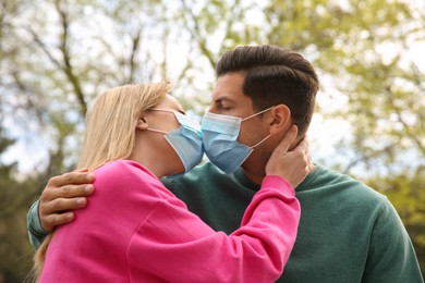 Photo of Couple in medical masks trying to kiss outdoors
