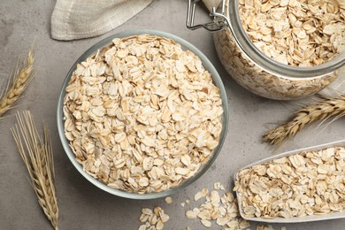 Photo of Oatmeal, glass bowl, jar and scoop on grey table, flat lay