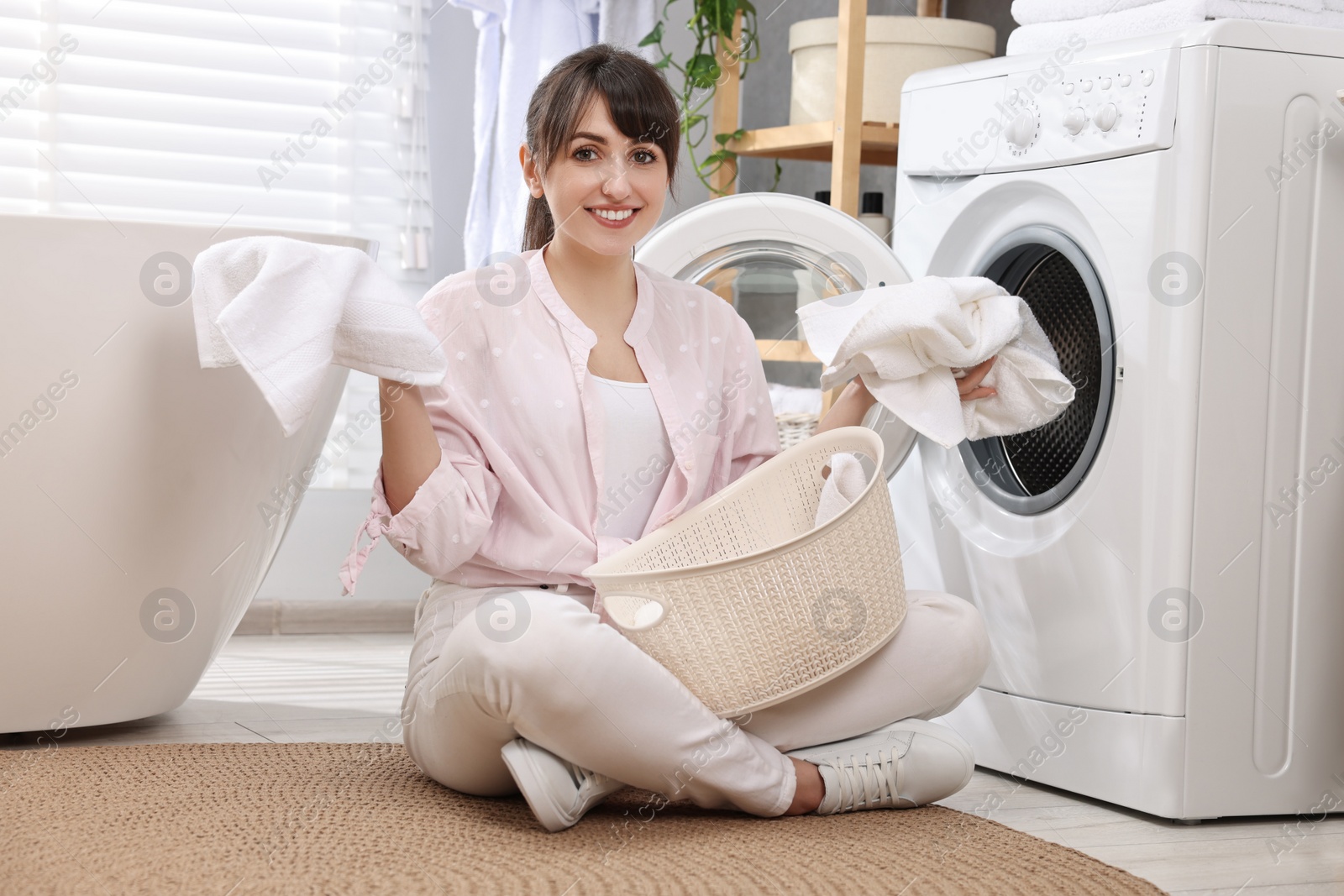 Photo of Happy young housewife with laundry near washing machine at home