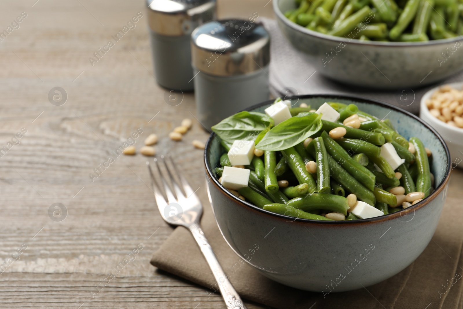 Photo of Delicious salad with green beans, pine nuts and cheese served on wooden table. Space for text