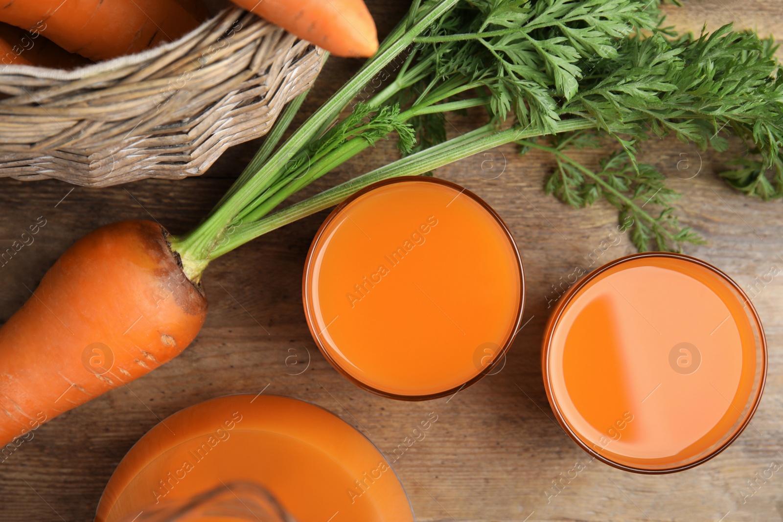 Photo of Freshly made carrot juice on wooden table, flat lay