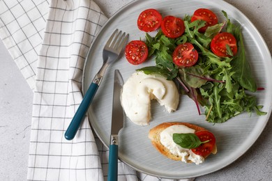 Delicious burrata cheese with tomatoes, arugula and toast served on grey table, top view