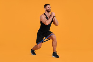 Photo of Young man exercising with elastic resistance band on orange background