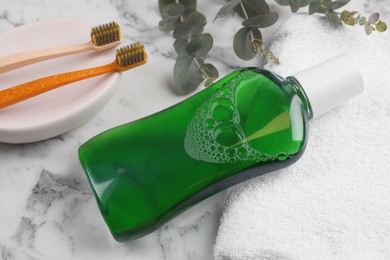 Photo of Fresh mouthwash in bottle, toothbrushes and towel on white marble table, closeup