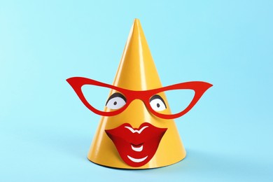 Photo of Handmade party hat with funny face on light blue background