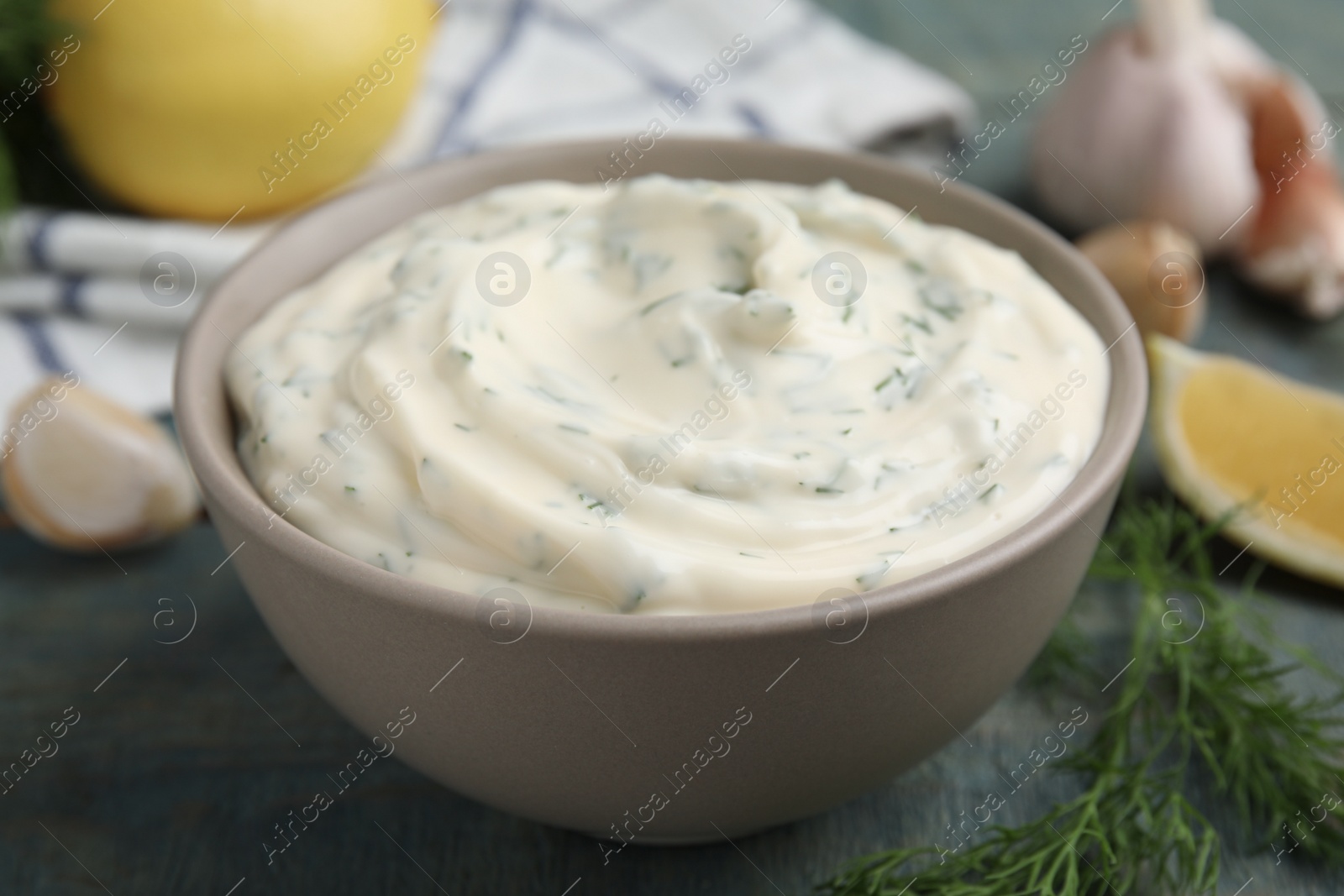 Photo of Tasty creamy dill sauce in bowl on blue wooden table, closeup