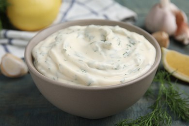 Tasty creamy dill sauce in bowl on blue wooden table, closeup