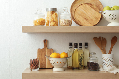 Photo of Wooden shelves with dishware and products on white wall. Kitchen interior idea